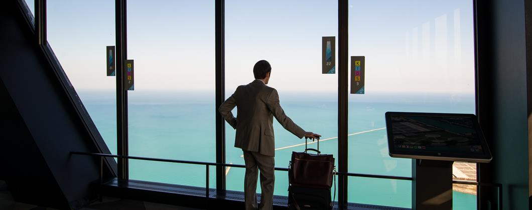 Smartly dressed man stood in an airport window with a suitcase and laptop bag. 