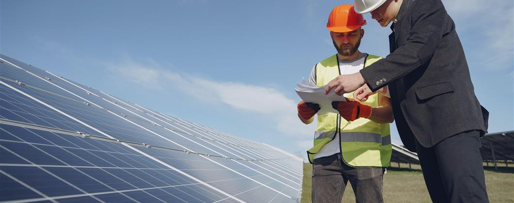 Two workers, one wearing high-viz and the other in a suit, inspecting paperwork on a worksite.