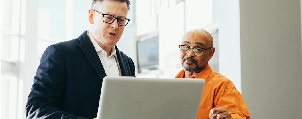 Businessmen discussing information on a laptop screen.