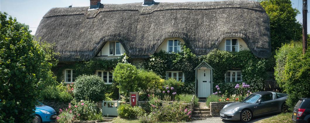 Line of thatched properties with cars parked outside.